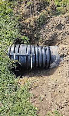 Large black corrugated drainage pipe being installed in a trench
